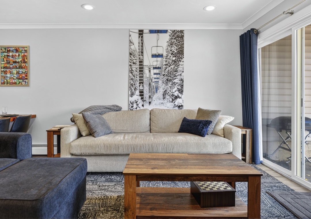 Settle into your inviting living room where a plush sofa and modern décor create a welcoming retreat. Natural light flows through glass doors, perfect for unwinding after mountain adventures.