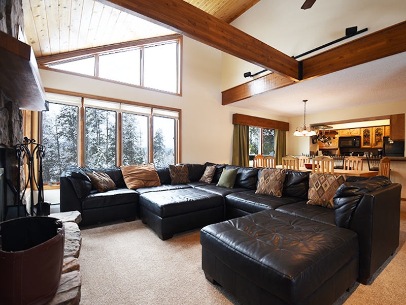 Unwind in your spacious living room with plush leather seating, soaring ceilings, and stunning forest views through expansive windows.