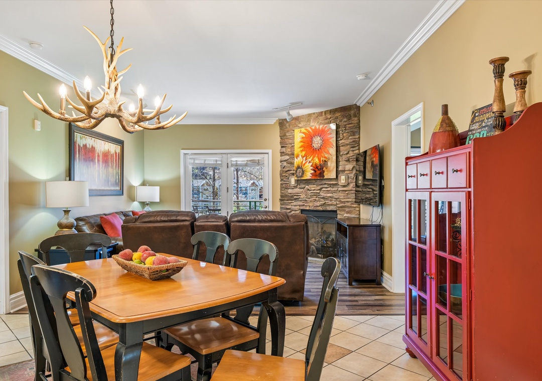 Gather around your dining table beneath the rustic antler chandelier, while the stone fireplace creates a cozy atmosphere for memorable meals.