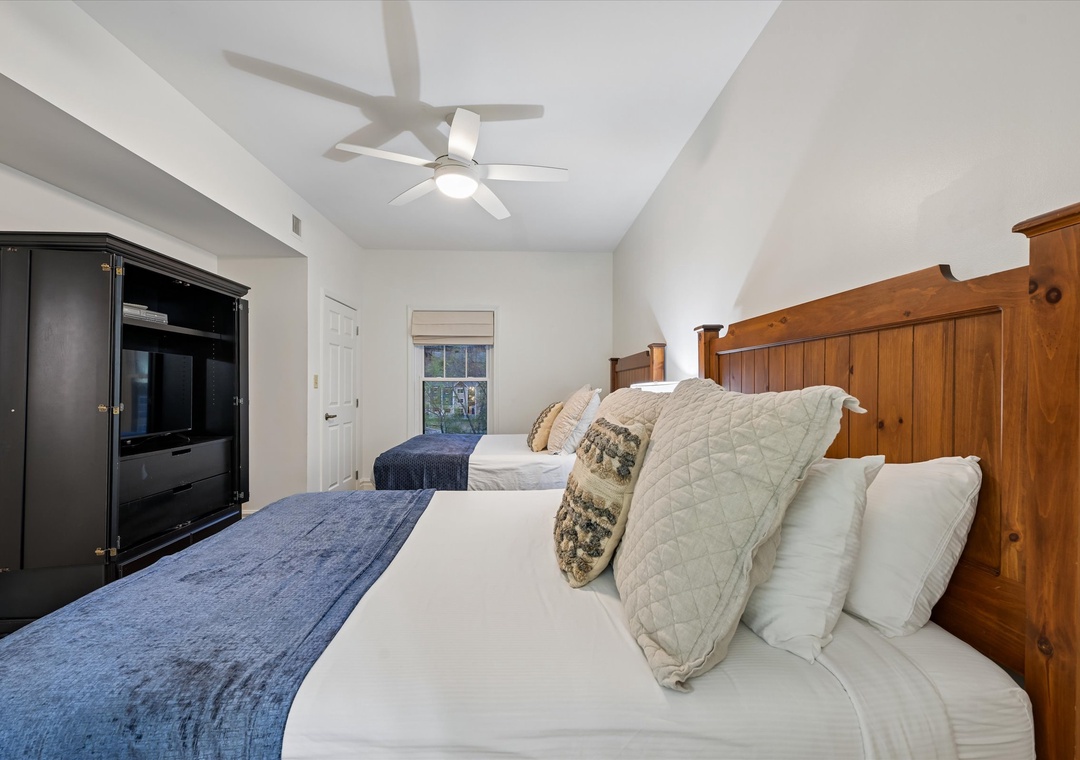 Unwind in your cozy twin bedroom with rustic wooden headboards, ceiling fan, and entertainment center for comfortable evenings.