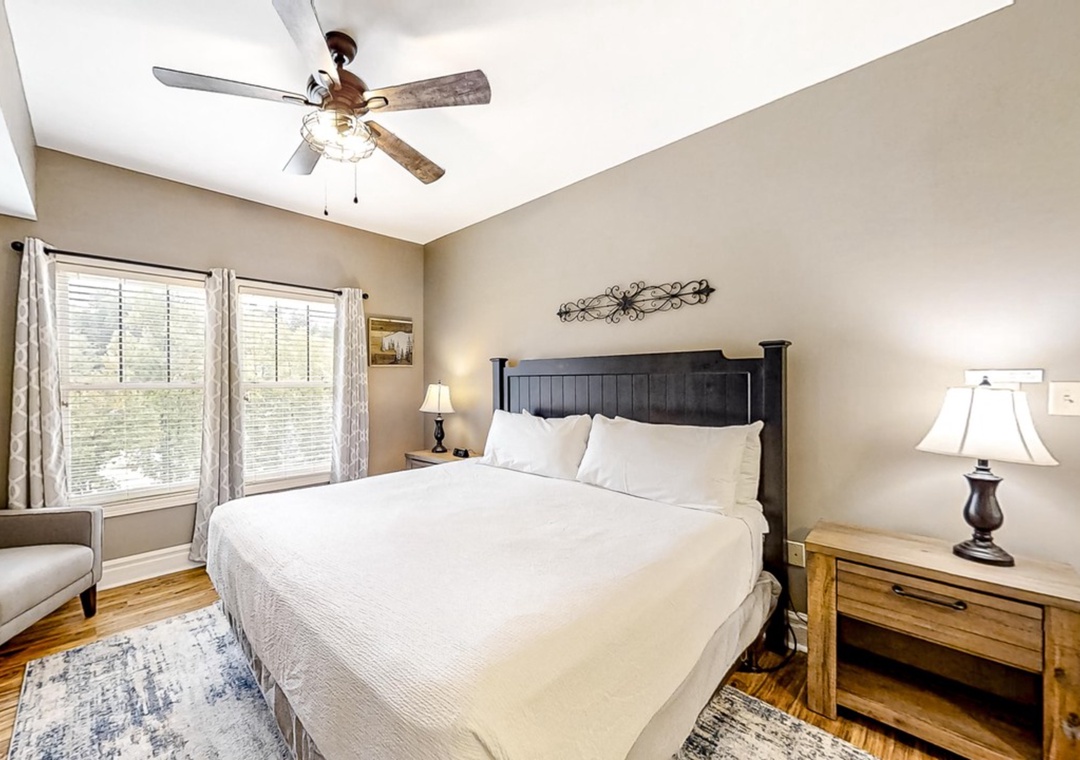 Drift off in this serene bedroom with crisp white linens, natural light filtering through blinds, and a gentle ceiling fan overhead.