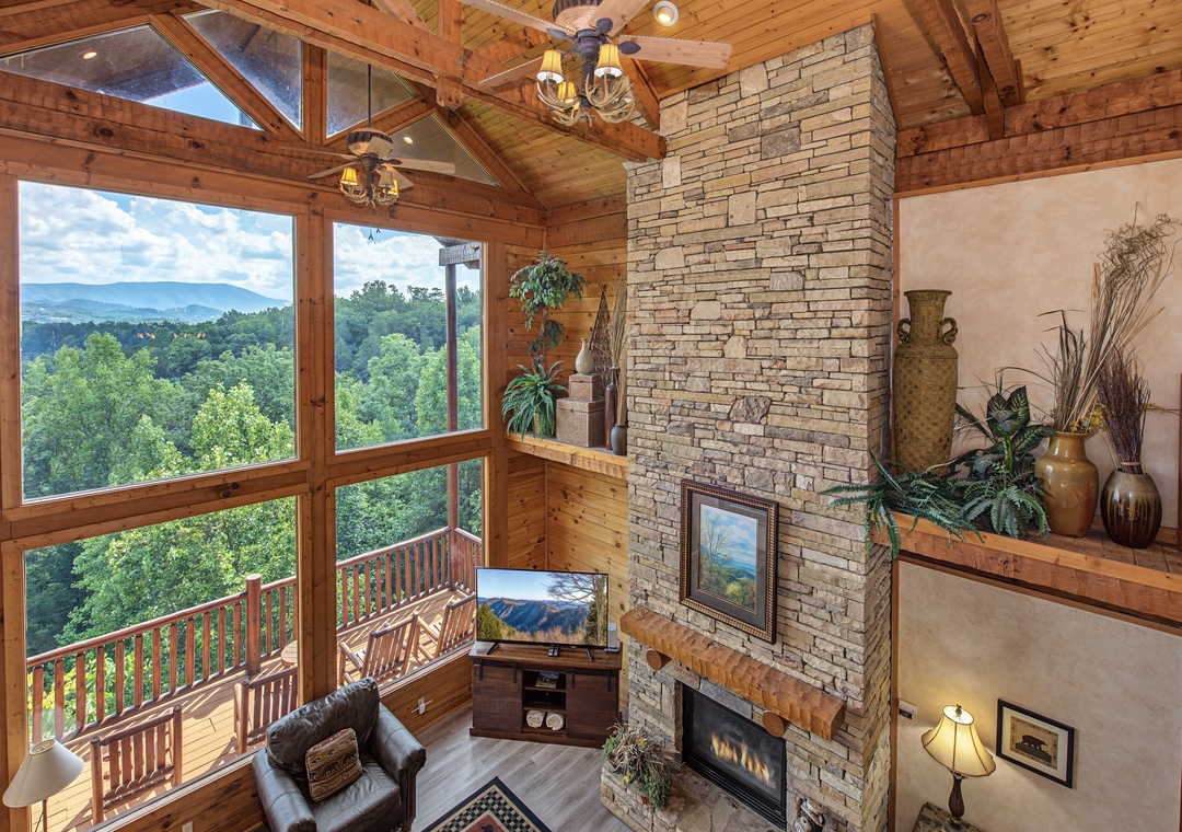 Settle into your cozy living room where floor-to-ceiling windows frame stunning mountain and forest views. The stone fireplace adds warmth while natural light pours through the soaring vaulted ceilings.