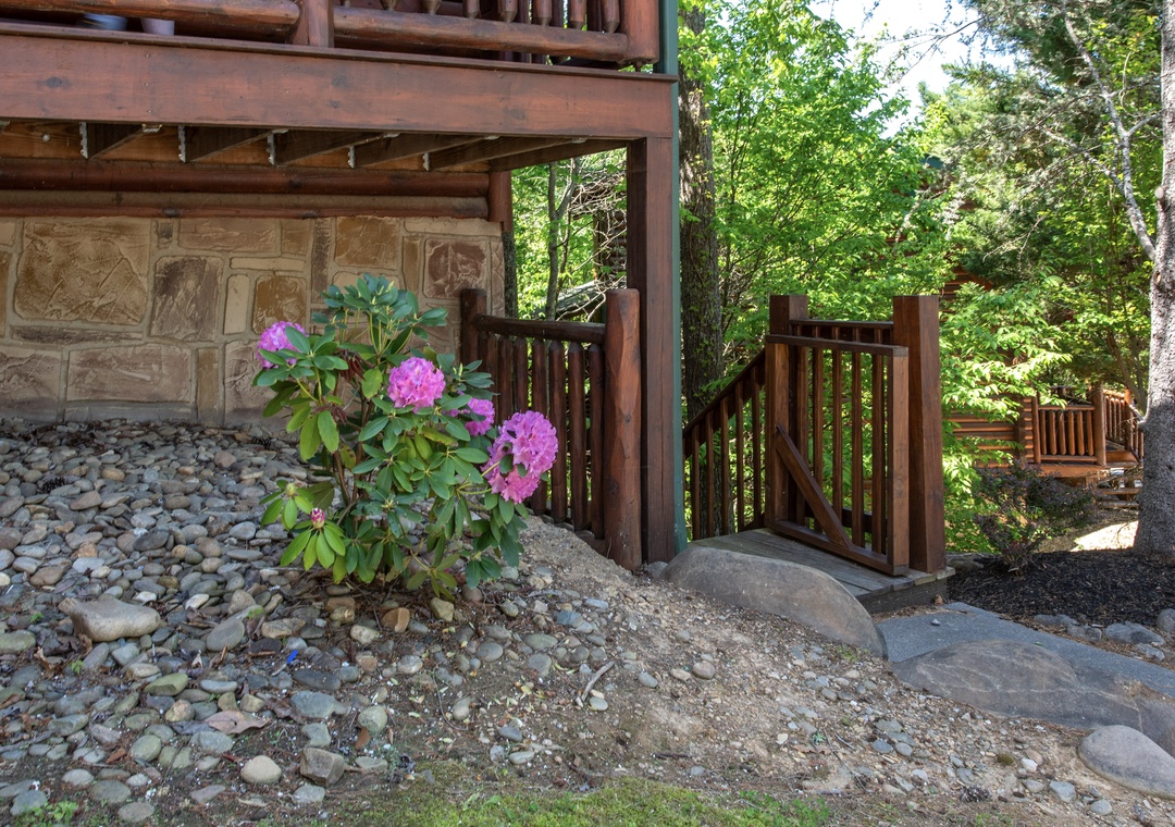 Charming wooden bridge leads through lush forest to your private retreat, surrounded by blooming rhododendrons and natural stone landscaping.