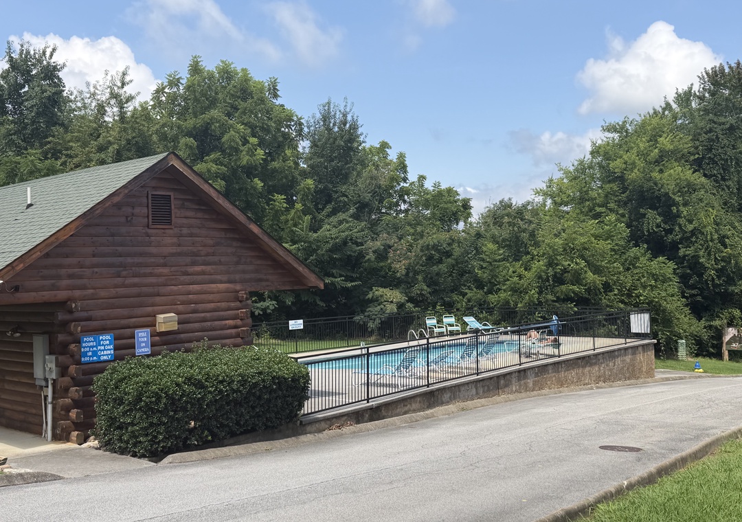 The property features a charming log cabin structure beside an inviting outdoor swimming pool, surrounded by lush greenery and mature trees in a peaceful natural setting.
