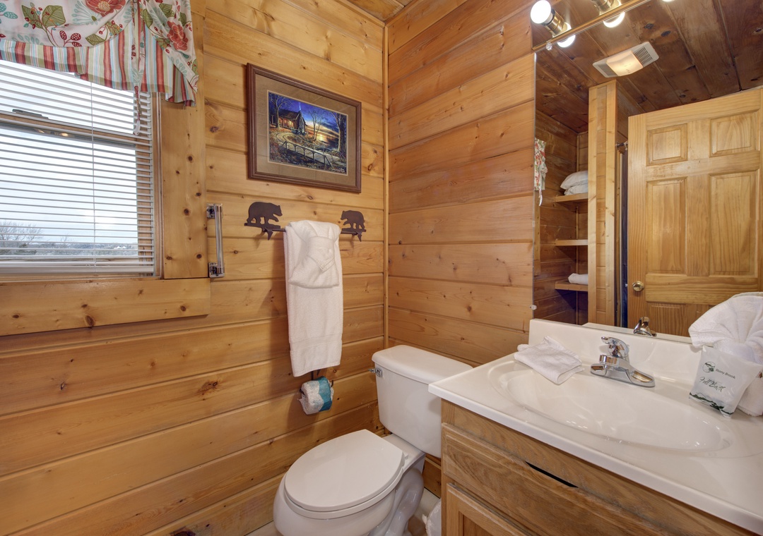 Your rustic bathroom features warm wood walls, fluffy towels, and charming bear-themed accents for a cozy mountain retreat experience.