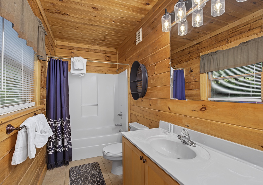 Freshen up in this warm cabin-style bathroom with fluffy towels, a full tub-shower combo, and rustic wood details that make every stay feel like a peaceful retreat.