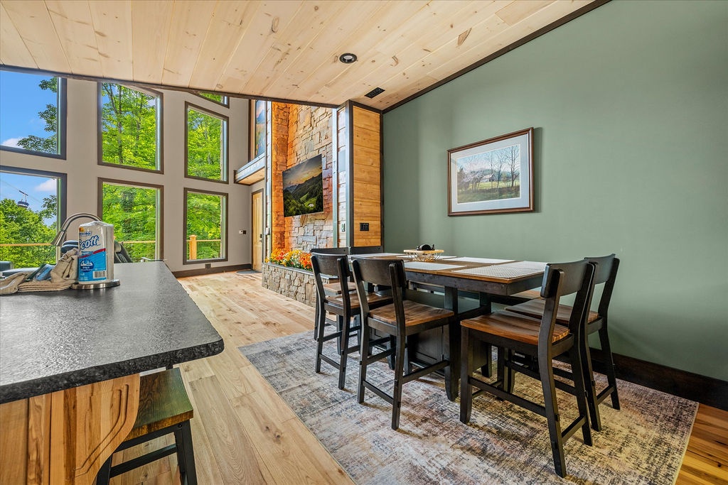 Share meals at this rustic dining table bathed in natural light from expansive windows, with a stunning stone fireplace adding warmth and mountain charm to your gathering space.