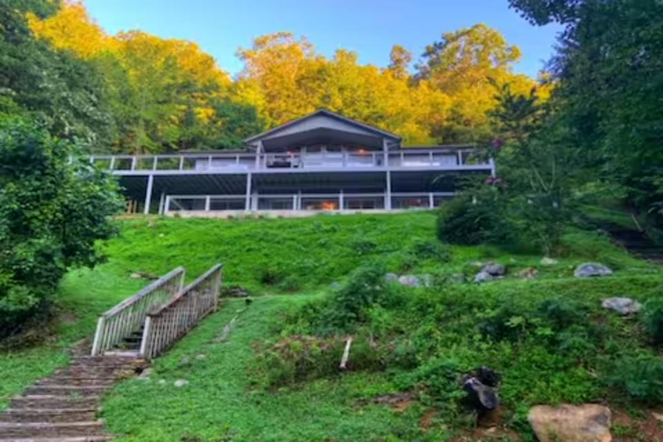 Modern lakeside retreat nestled among vibrant autumn foliage, featuring elevated deck and peaceful woodland setting.
