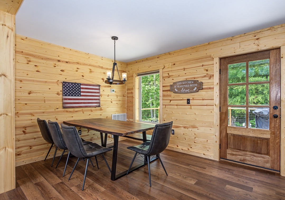 Gather around this rustic dining table where memories are made, with warm wood-paneled walls and natural light pouring in from the windows, creating the perfect setting for your meals together.