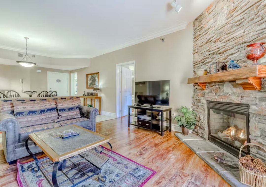 Sink into your cozy living room with rustic stone fireplace, where warm wood floors and mountain-themed decor create the perfect retreat.