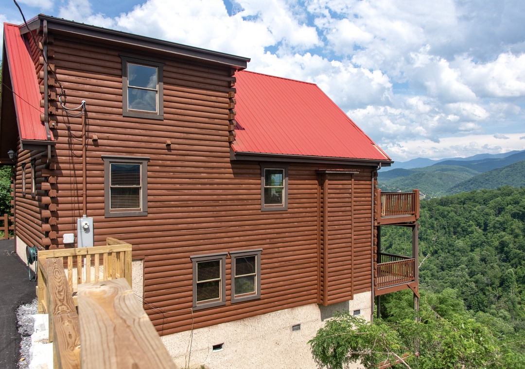A spacious mountain cabin with a distinctive red metal roof nestled among the lush, rolling peaks—offering a peaceful retreat surrounded by nature's beauty.