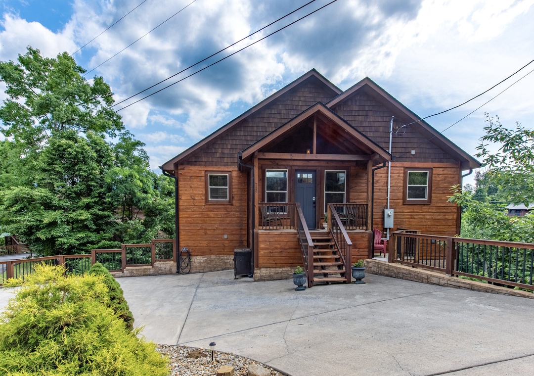 A charming cedar cabin with a welcoming covered porch and gabled roofline, set among lush green trees with ample parking for your mountain getaway.