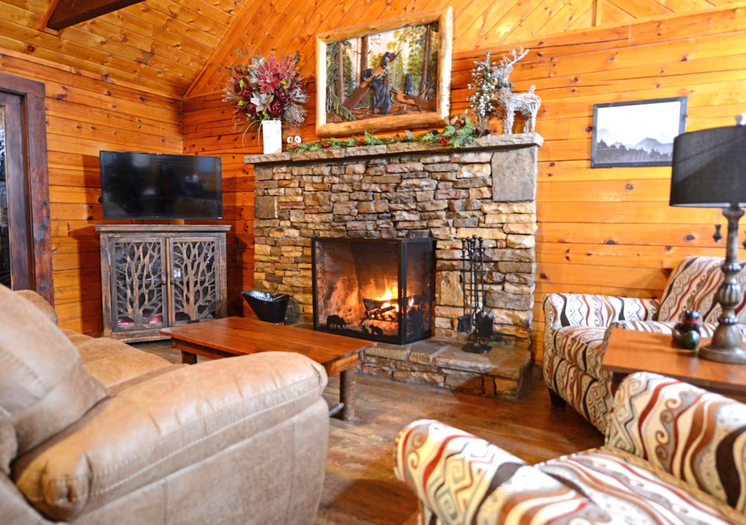 Cozy up by your crackling stone fireplace in this warm cabin living room, complete with comfy seating and rustic charm.