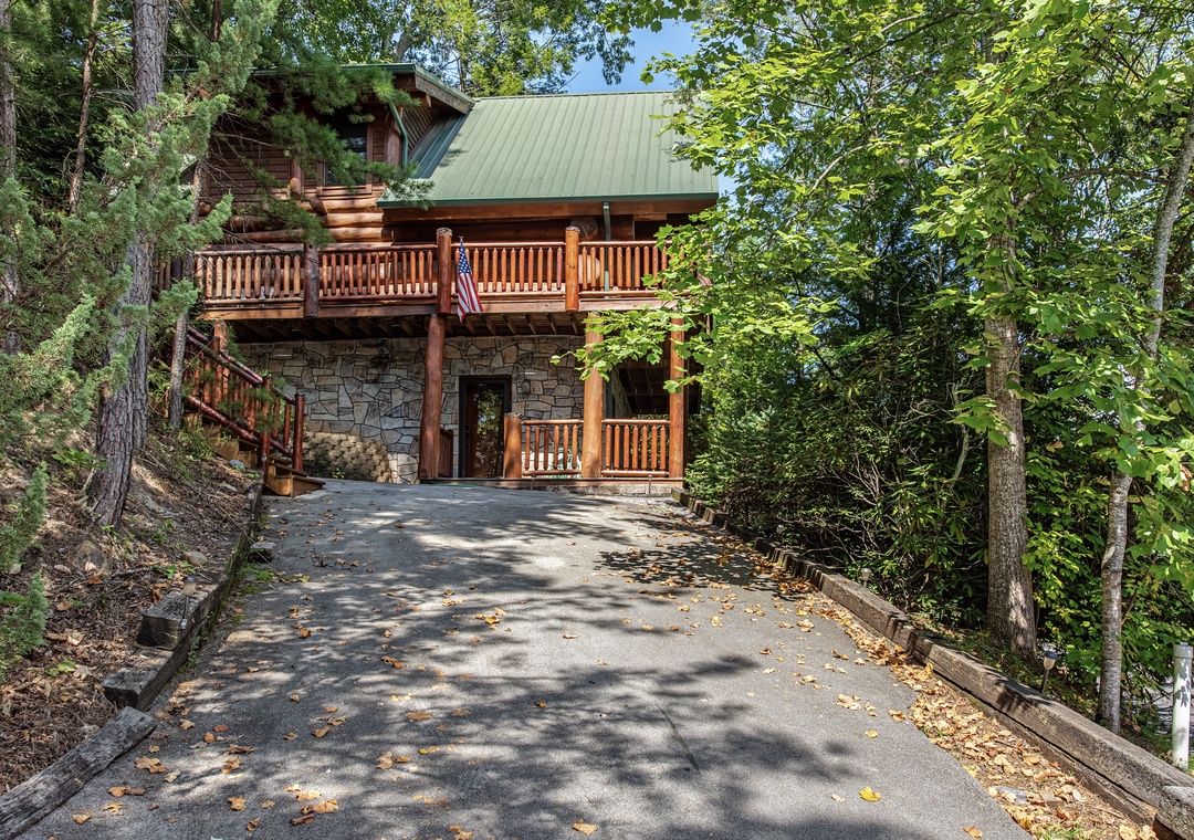 A secluded log cabin nestled among towering trees, featuring charming wood balconies and a stone foundation. This peaceful mountain retreat offers easy parking and multiple outdoor spaces for relaxation.