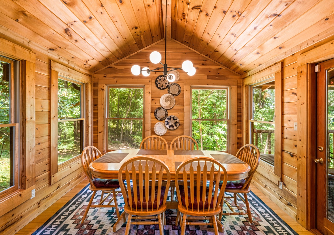 Gather around this warm wood dining space where natural light pours through floor-to-ceiling windows, bringing the peaceful forest right to your table for memorable meals together.