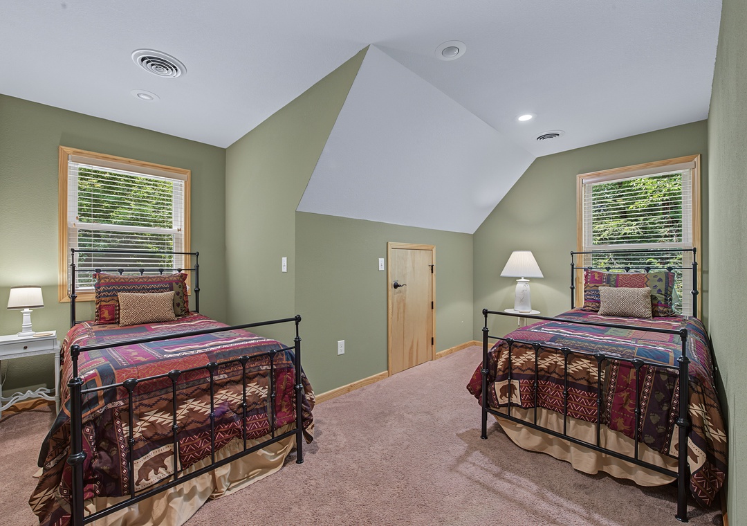 Relax in this charming twin bedroom, where sage walls meet natural light from two windows and vaulted ceilings create an airy, peaceful retreat perfect for restful nights.