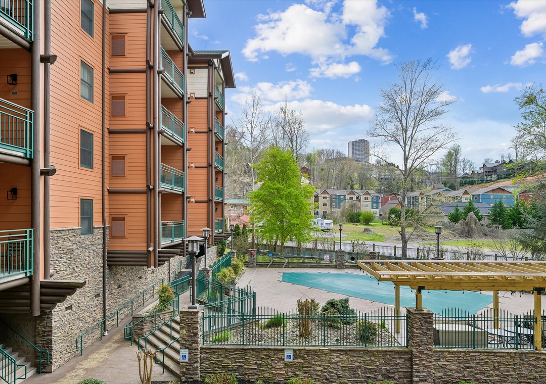 Multi-story property building overlooking a sparkling pool in a scenic neighborhood setting with city skyline views.