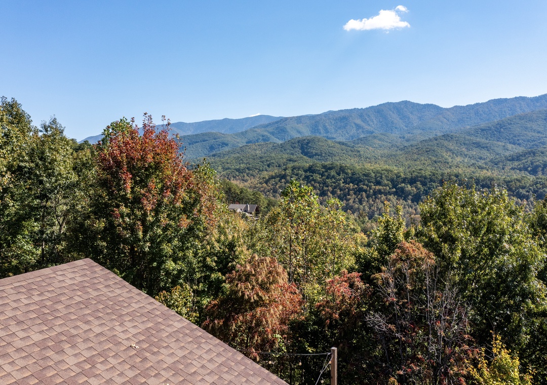 The property overlooks a stunning mountain landscape framed by forested hills and brilliant blue skies, with touches of autumn color appearing in the surrounding trees.