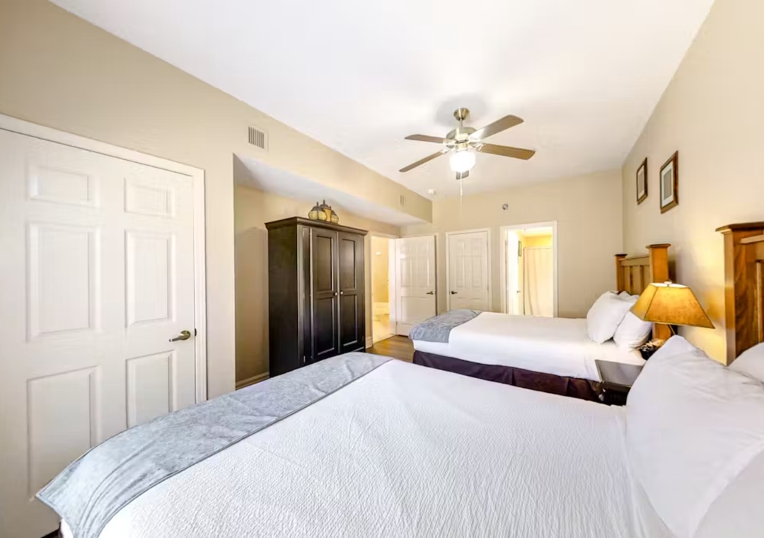 Rest peacefully in your spacious twin bedroom with plush linens, warm wood furnishings, and gentle ceiling fan creating the perfect sleep sanctuary.