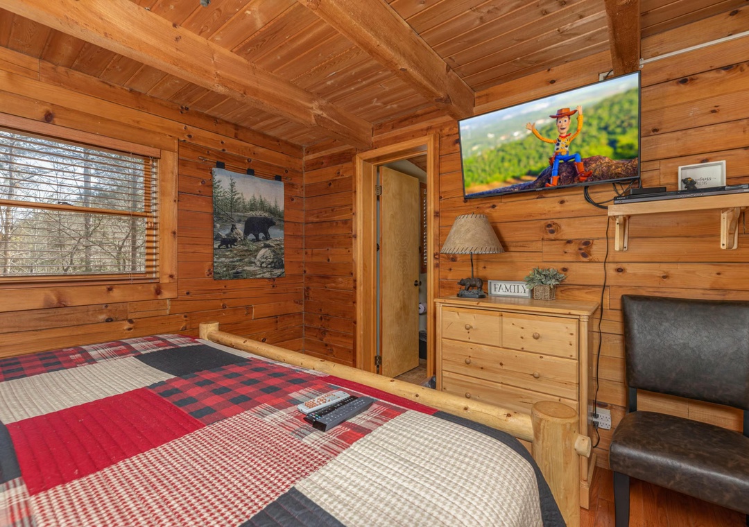 Settle into your cozy log bedroom with rustic charm and modern comforts, featuring a plush bed and warm wooden beams overhead.