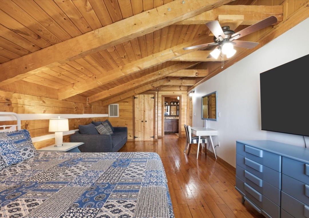 Unwind in your cozy cabin loft with rustic wood beams overhead, a plush bed, and modern entertainment system for perfect mountain getaway relaxation.