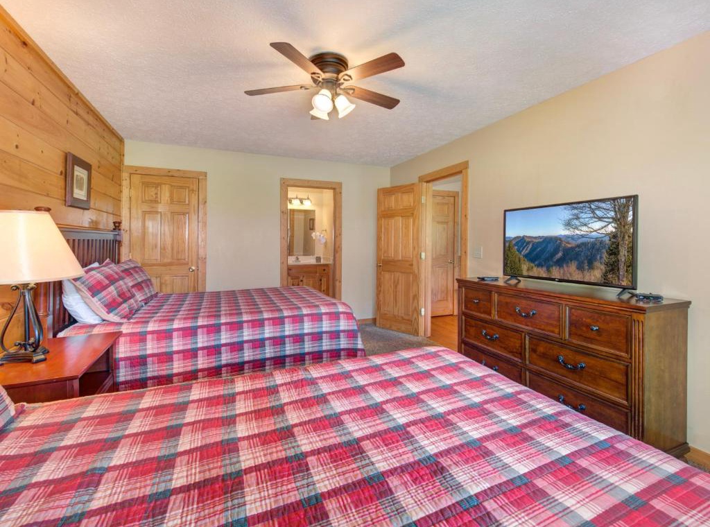 Cozy mountain retreat bedroom with twin beds, warm wood accents, and flat-screen TV for your evening relaxation.