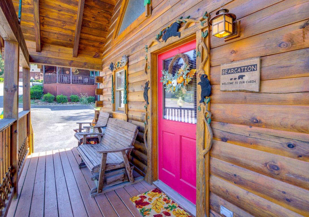 Charming log cabin entrance with bright red door and rustic porch seating welcomes you to your mountain retreat.