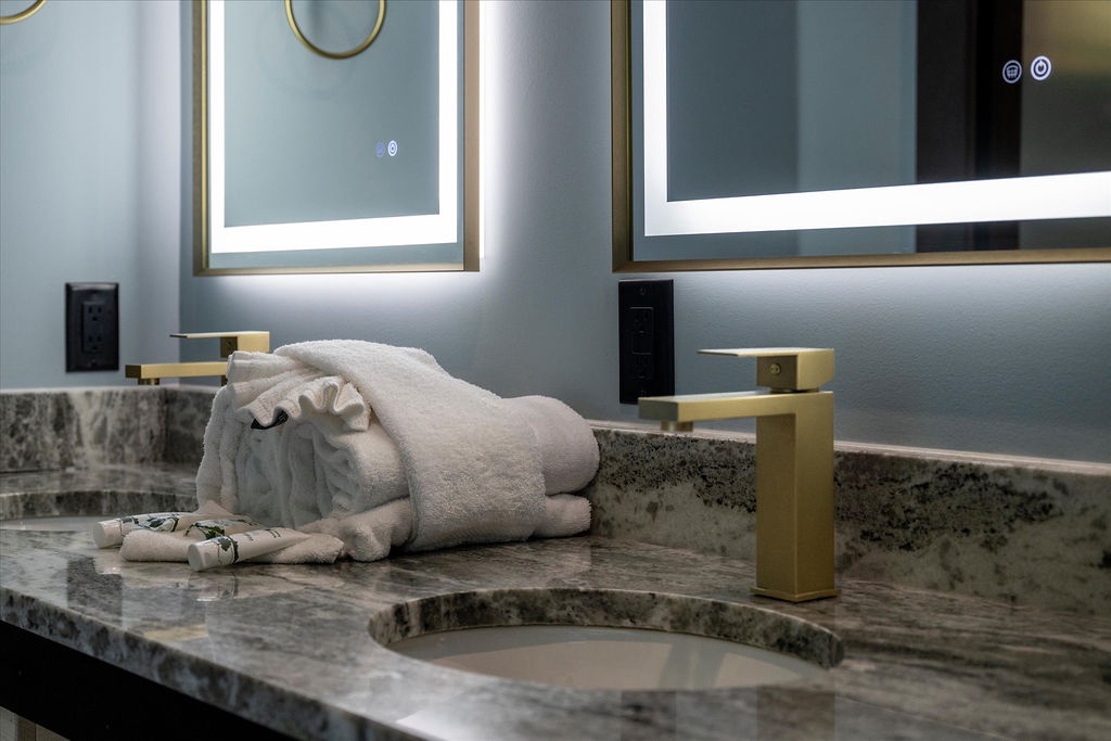 Step into your spa-like bathroom where elegant marble surfaces meet warm ambient lighting. Fresh towels and premium amenities await your arrival, all wrapped in a serene palette of soft grays and luxe gold accents.
