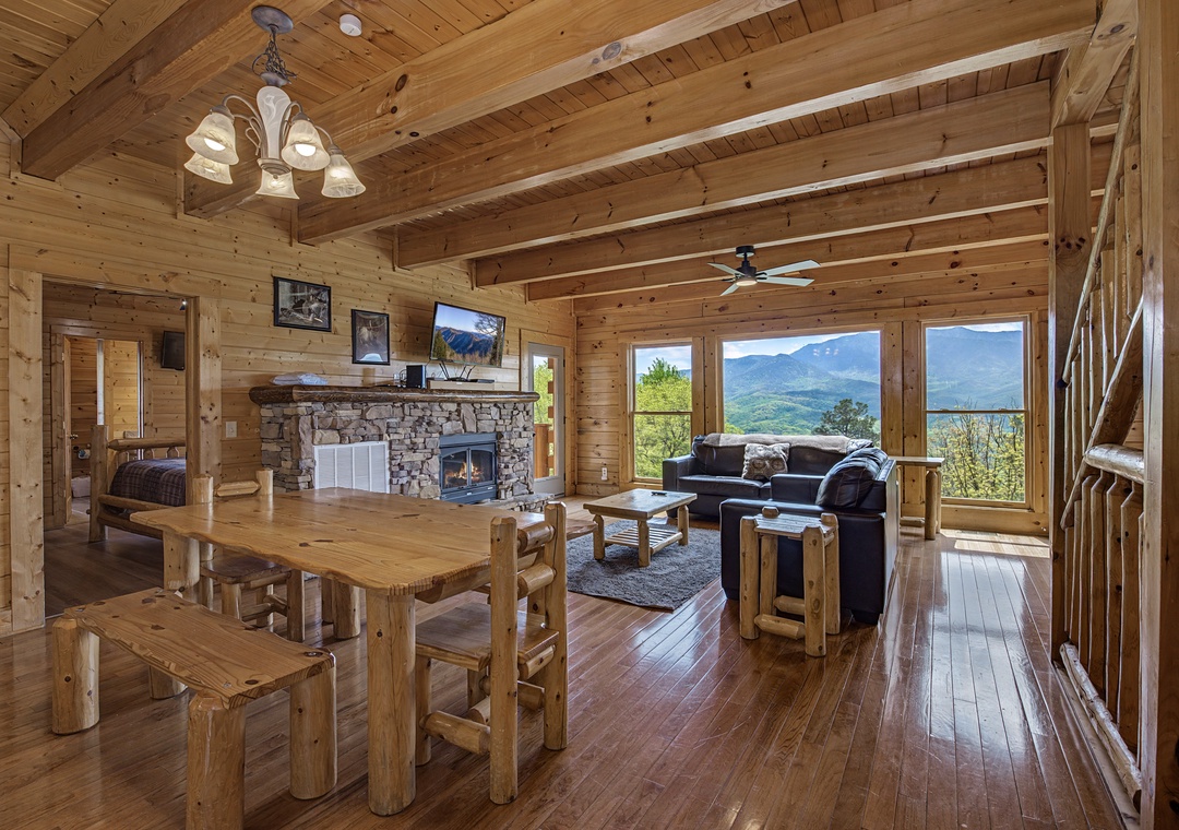 Unwind in your cozy mountain cabin with rustic wood beams, stone fireplace, and stunning valley views through expansive windows.