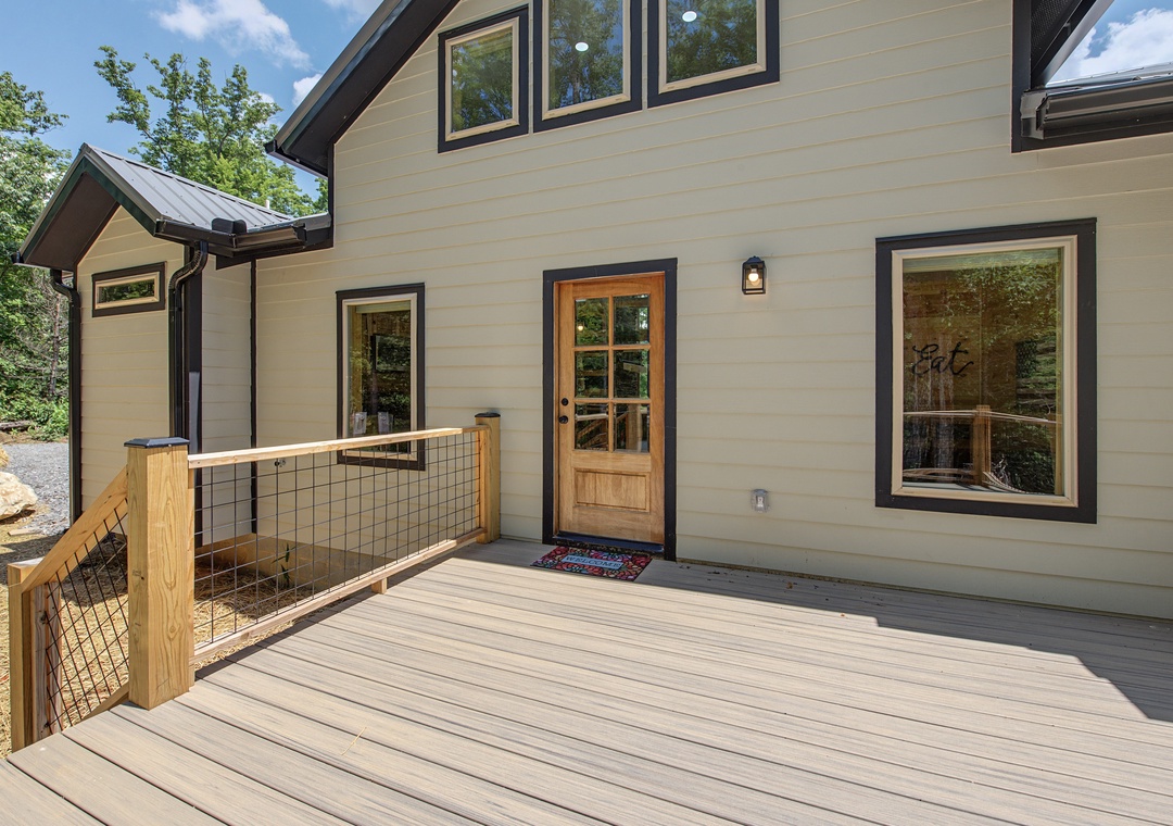 Warm welcome to your mountain retreat with a charming wooden door, spacious deck, and lush greenery surrounding you. Modern farmhouse style blends perfectly with the peaceful wooded setting.