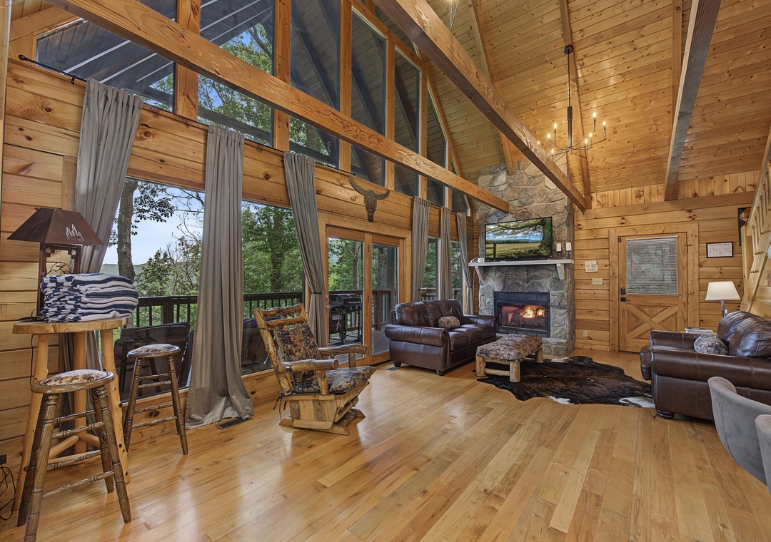 Gather around the warmth of your wood-burning fireplace in this open-concept living space, where soaring cathedral ceilings, exposed beams, and floor-to-ceiling windows invite you to unwind surrounded by nature.