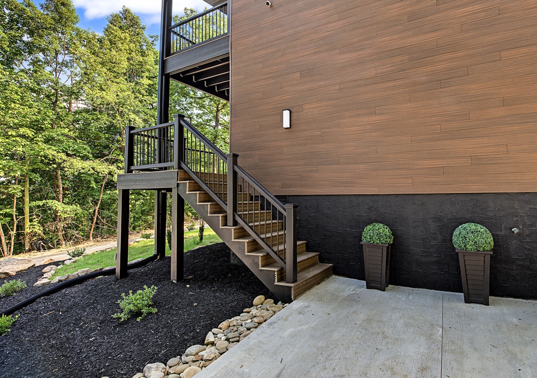 Modern architectural exterior featuring dark stone accents, warm wood paneling, and thoughtfully landscaped surroundings with decorative planters and natural greenery.