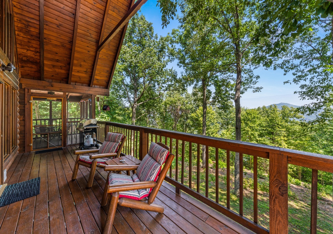 A peaceful mountain-view deck awaits in this forested hillside setting, framed by tall trees and surrounded by summer greenery beneath clear blue skies.
