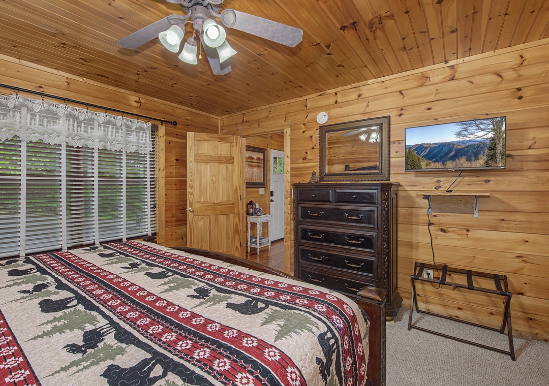 Settle into rustic comfort with a cozy cabin bedroom featuring wood-paneled walls, a ceiling fan, and stunning mountain views framed in your window—your peaceful retreat awaits.