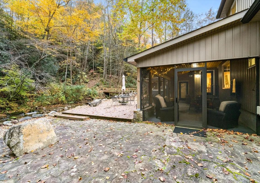 A private outdoor retreat where natural stone pathways lead through vibrant fall foliage to your covered patio and bubbling stream, blending modern comfort with woodland serenity.