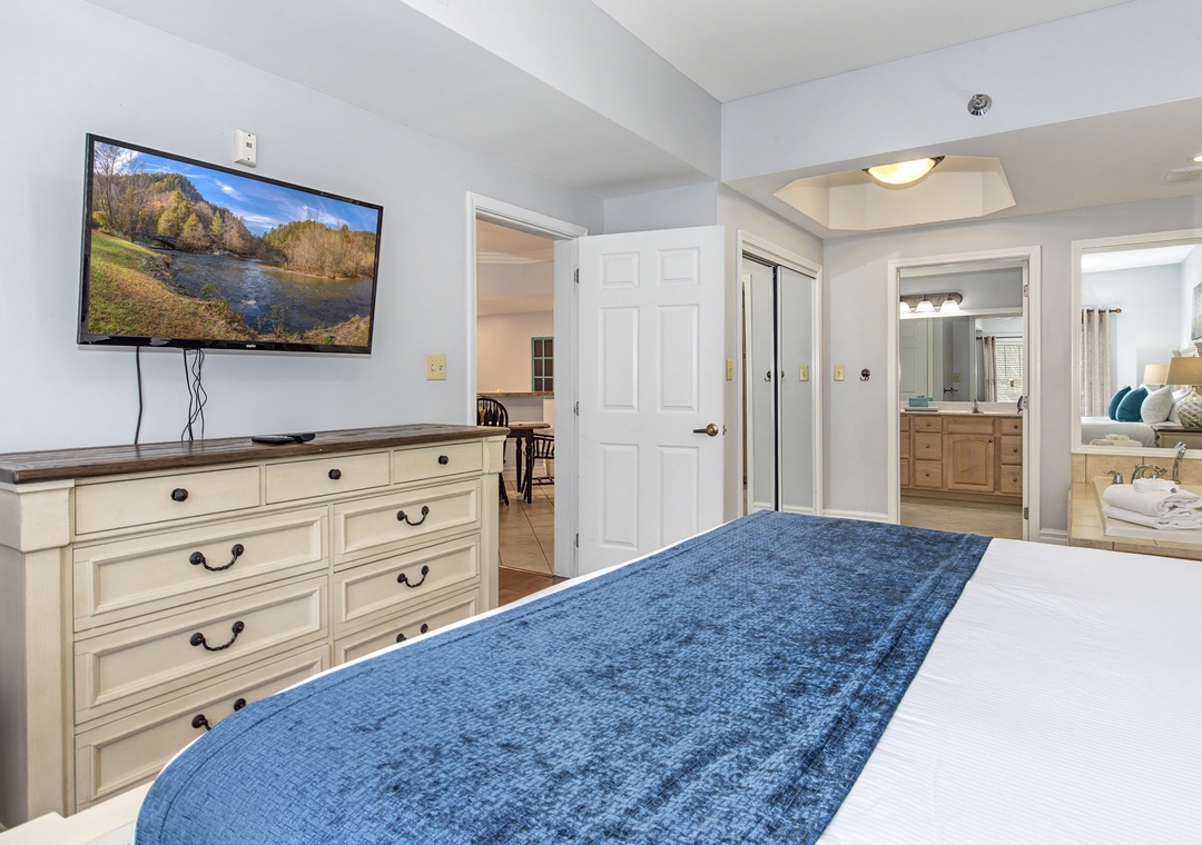 Unwind in your spacious bedroom featuring a wall-mounted TV, elegant dresser, and glimpse of the en-suite bathroom.