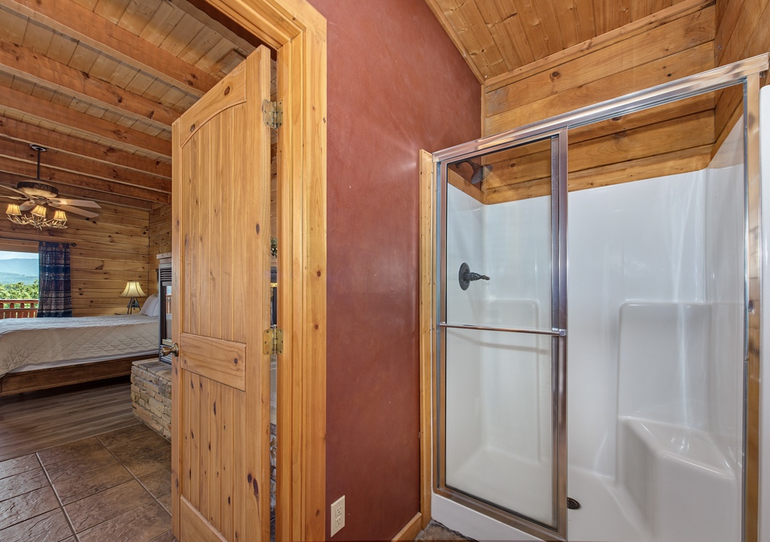 Step into your rustic retreat where warm wood paneling wraps every surface in mountain charm. Your private shower awaits behind frosted glass doors, while your bedroom beckons just beyond the arched doorway.