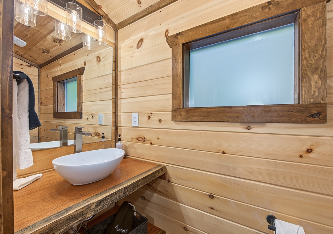 Your rustic bathroom features natural wood walls, a modern vessel sink on a reclaimed wood vanity, and soft lighting that creates a cozy cabin feel.