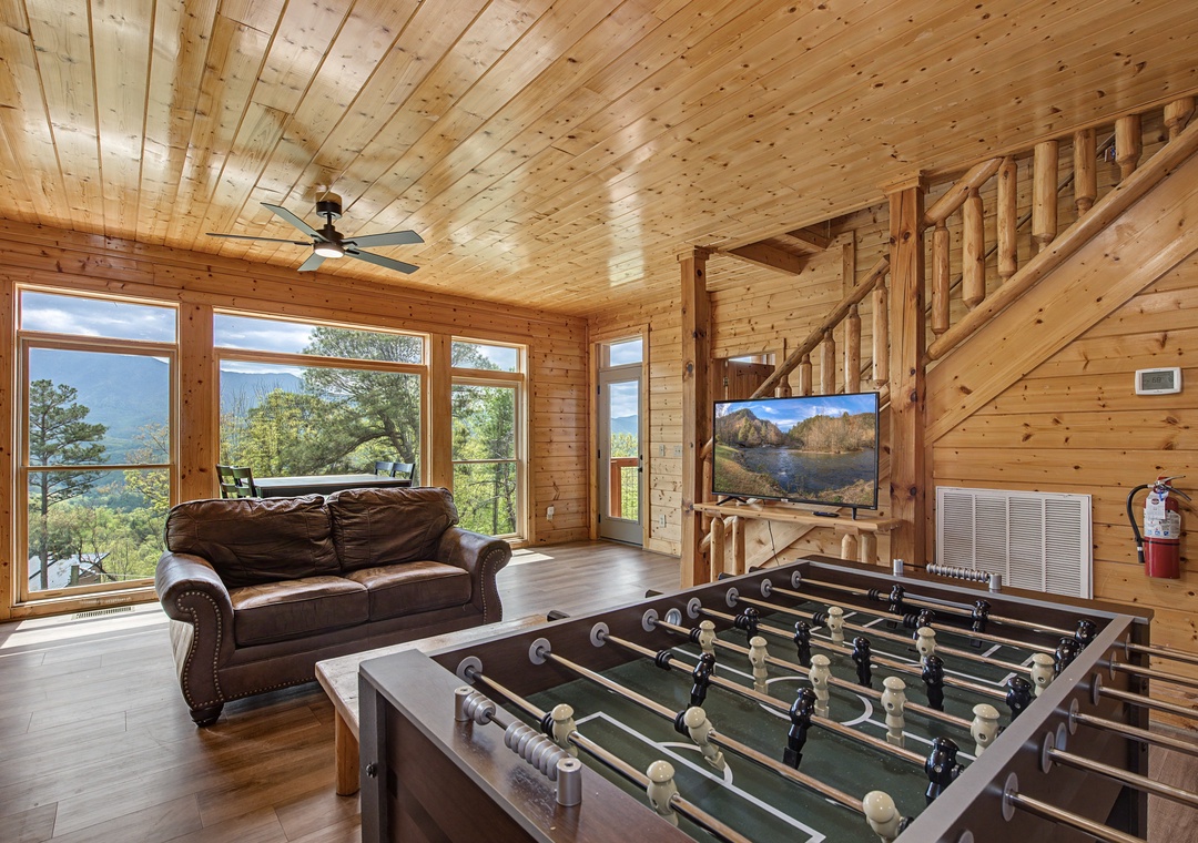 Your mountain retreat's game room features foosball, cozy seating, and stunning valley views through floor-to-ceiling windows.