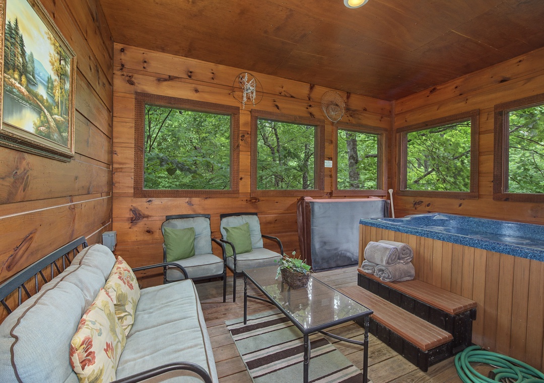 Unwind in your private screened porch with cozy seating and a hot tub, surrounded by lush forest views through wide windows—perfect for peaceful evenings.