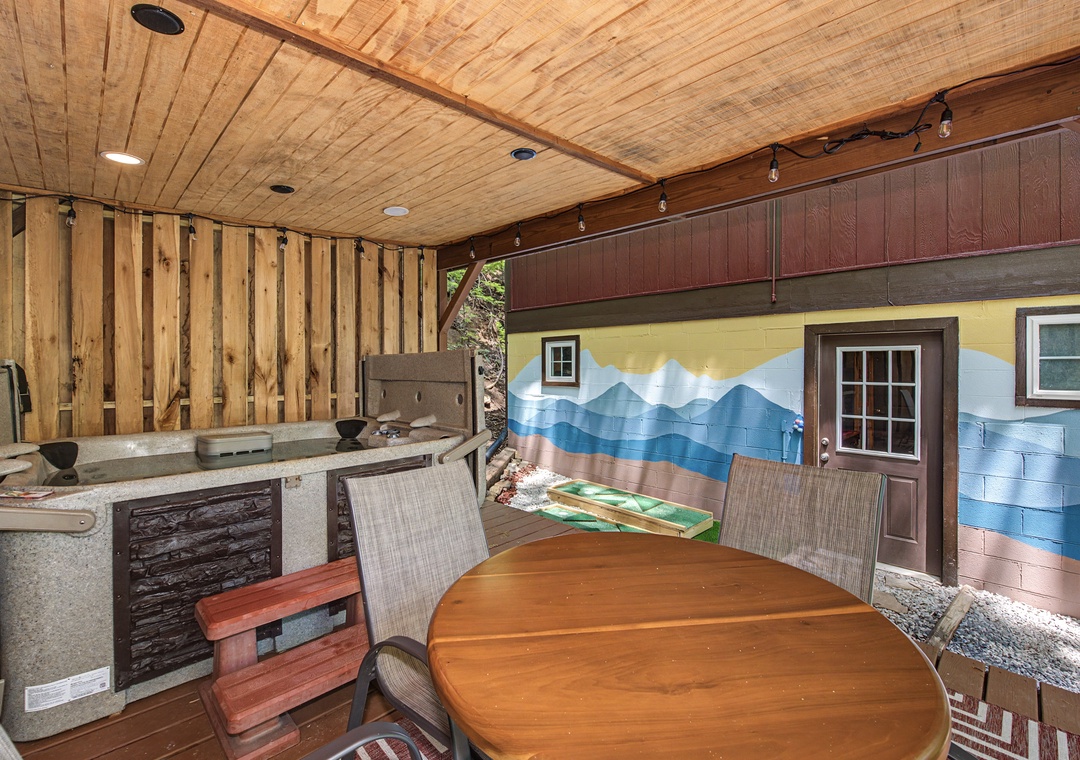 Step into your private covered patio featuring a hot tub, outdoor bar, and charming mountain mural—perfect for relaxing evenings under wood-beamed ceilings.