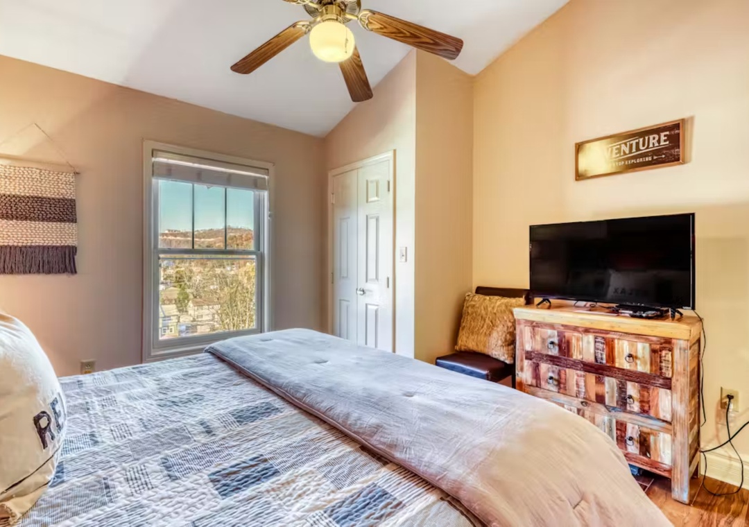 Unwind in your cozy bedroom with rustic charm, featuring a comfortable bed, ceiling fan, and TV for relaxing evenings.