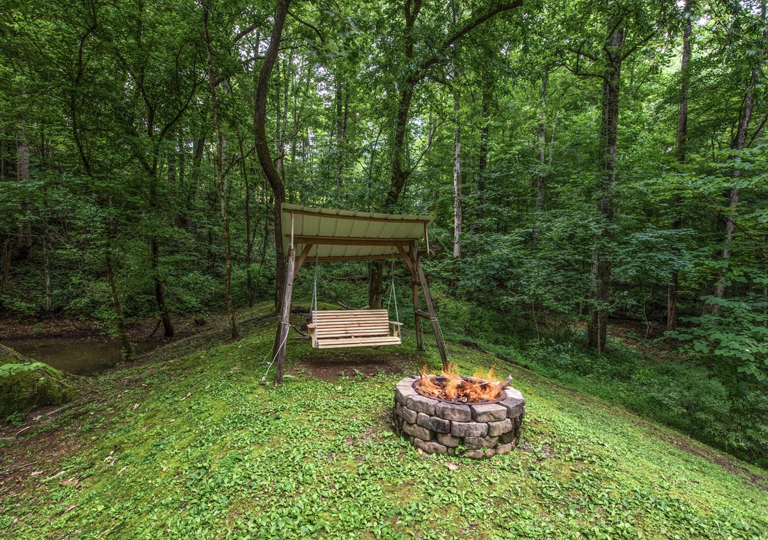 Swing gently under the canopy while flames crackle in the stone fire pit, surrounded by lush forest and a peaceful stream nearby.