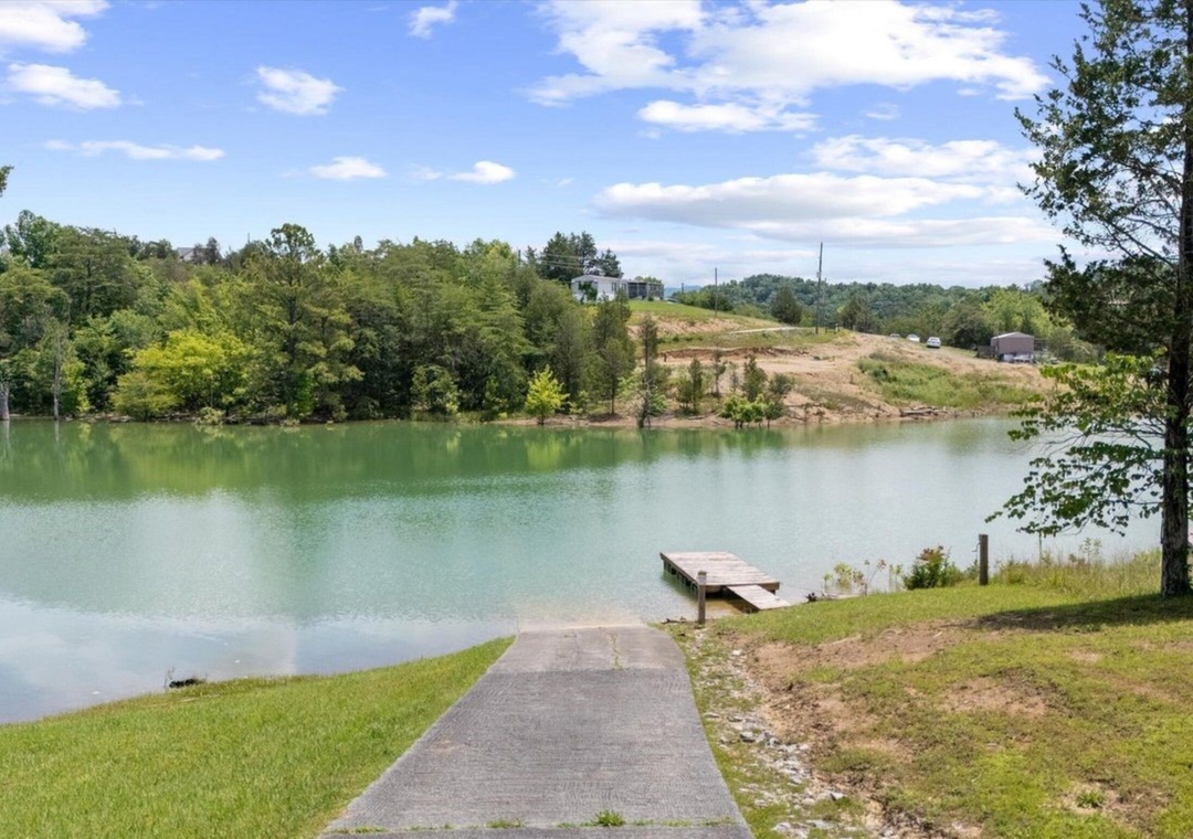 Tranquil lake setting with private dock access surrounded by lush trees and rolling hills.