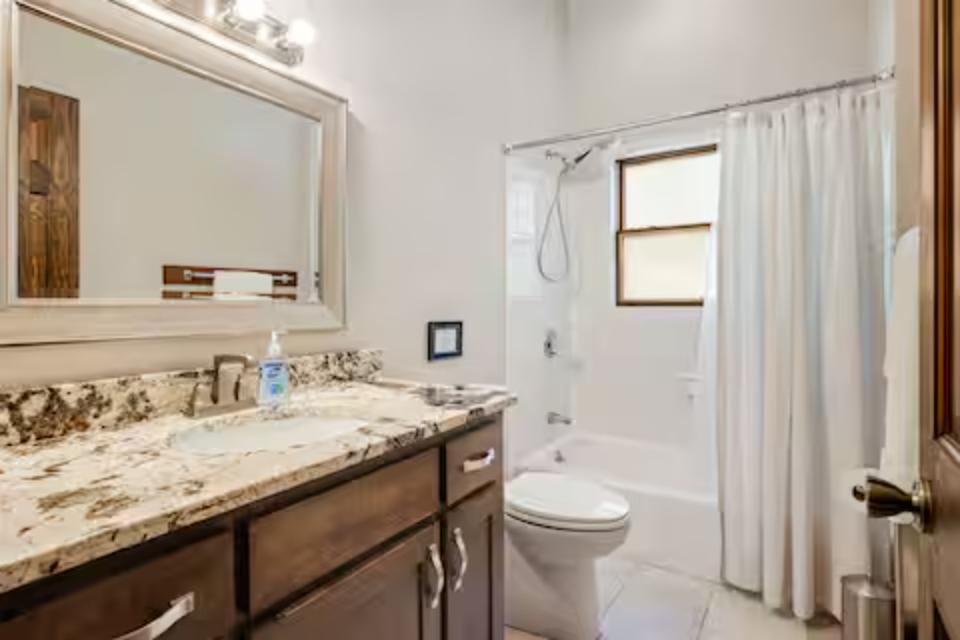 Refresh in your private bathroom featuring beautiful granite countertops, bright vanity lighting, and a spacious shower-tub combo.