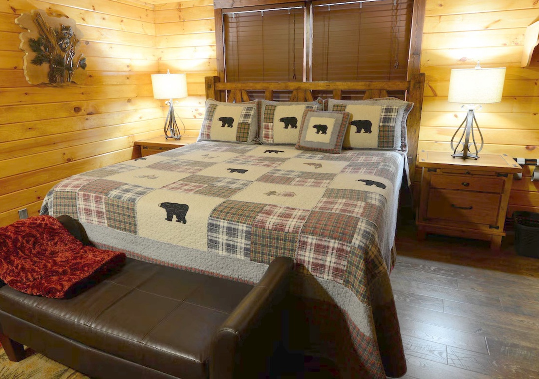 Cozy rustic bedroom with handcrafted log walls, bear-themed quilted bedding, and warm bedside lighting for your mountain retreat.