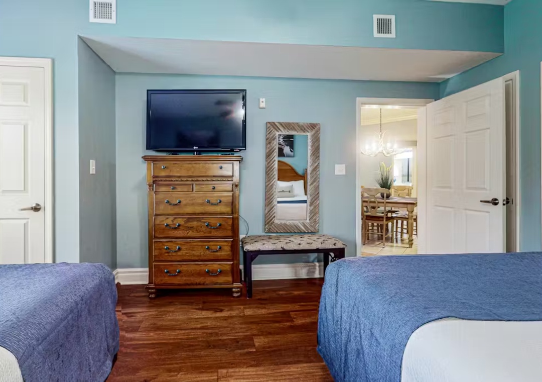 Relax in your peaceful twin bedroom with calming blue walls, rich hardwood floors, and modern amenities including flat-screen TV.