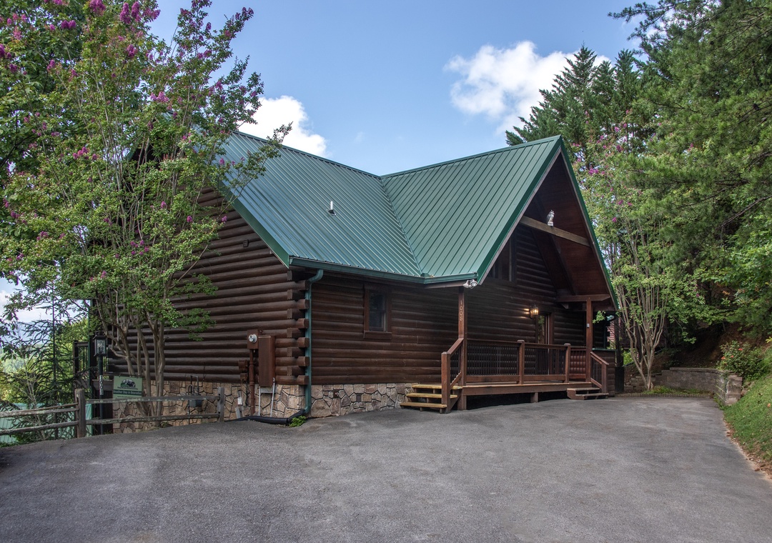 Charming log cabin nestled among blooming trees and lush forest, featuring rustic wood construction with modern green metal roofing and welcoming front entrance.