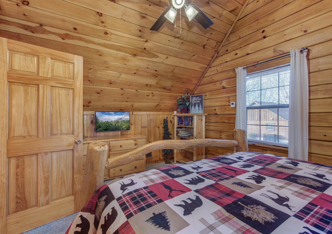 Cozy cabin bedroom with rustic log walls, built-in entertainment center, and charming wildlife-themed bedding for your mountain getaway.