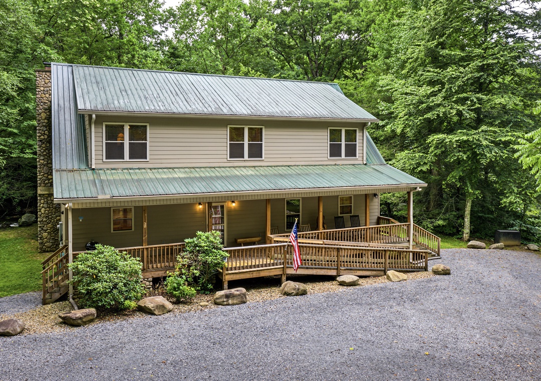 A charming two-story home nestled among lush green trees with a welcoming covered front porch, stone chimney, and ample parking—your perfect retreat for a peaceful mountain getaway.